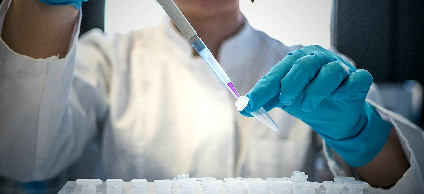 Mãos com luvas azuis manipulando pipeta em laboratório
